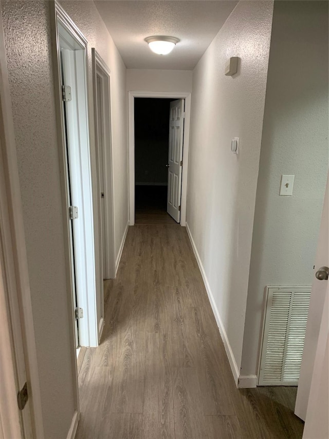 hall featuring visible vents, baseboards, wood finished floors, a textured wall, and a textured ceiling