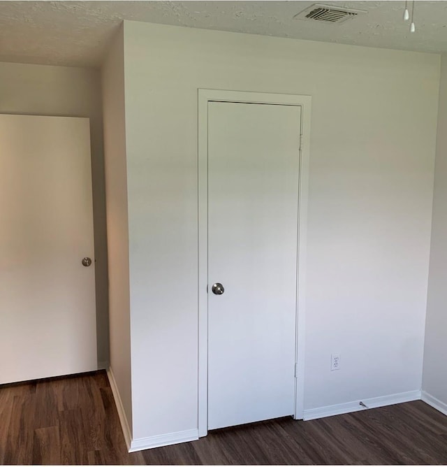 unfurnished bedroom featuring dark wood finished floors, visible vents, a textured ceiling, and baseboards