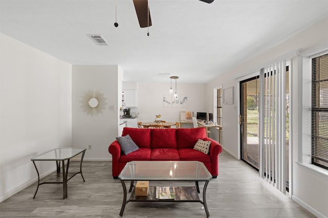 living room with ceiling fan, baseboards, visible vents, and light wood-type flooring