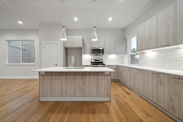 kitchen with a sink, light brown cabinets, stainless steel appliances, modern cabinets, and a kitchen island with sink