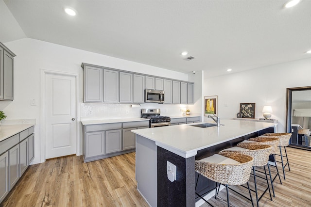 kitchen with gray cabinetry, stainless steel appliances, a kitchen breakfast bar, and a sink