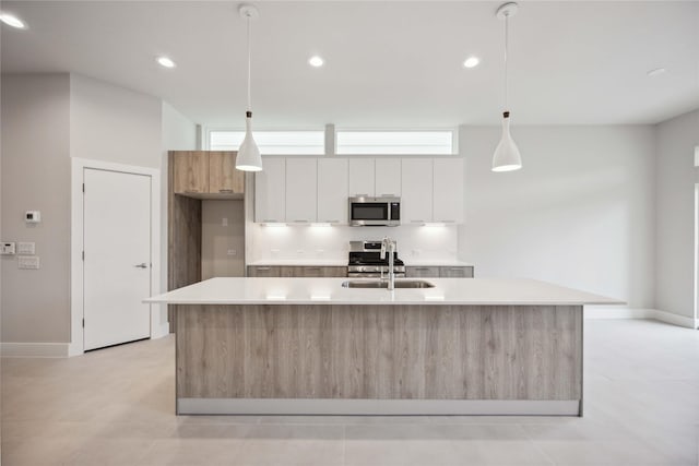 kitchen with a sink, stainless steel appliances, an island with sink, light countertops, and modern cabinets