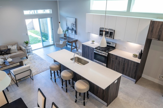 kitchen featuring a sink, a kitchen breakfast bar, modern cabinets, light countertops, and appliances with stainless steel finishes