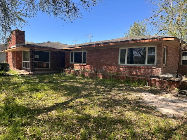 view of front of house with brick siding, a front lawn, and a chimney