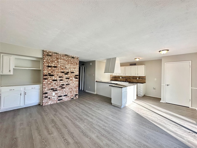 kitchen featuring light wood finished floors, wall chimney range hood, decorative backsplash, white cabinets, and a textured ceiling