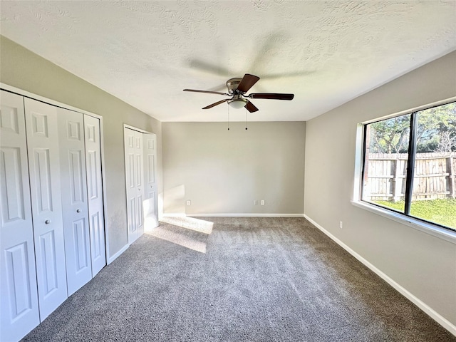 unfurnished bedroom featuring two closets, ceiling fan, baseboards, carpet floors, and a textured ceiling