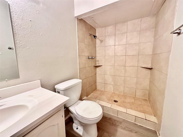 full bathroom featuring vanity, toilet, a textured wall, and tiled shower