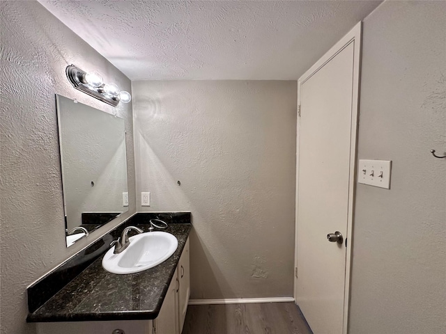 bathroom featuring vanity, wood finished floors, a textured wall, and a textured ceiling