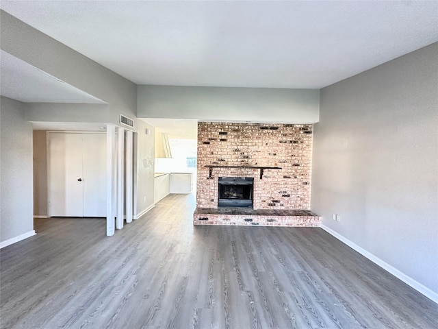 unfurnished living room featuring visible vents, baseboards, wood finished floors, and a fireplace