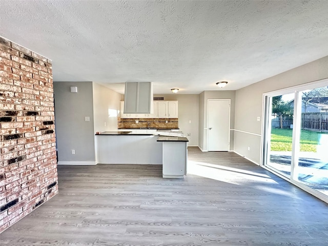 kitchen featuring dark countertops, wood finished floors, a peninsula, white cabinets, and decorative backsplash