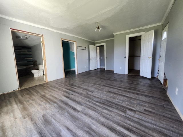 unfurnished bedroom with ornamental molding, a walk in closet, connected bathroom, and wood finished floors