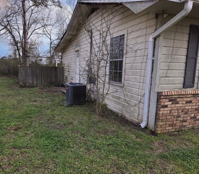 view of side of property featuring central AC, fence, and a yard