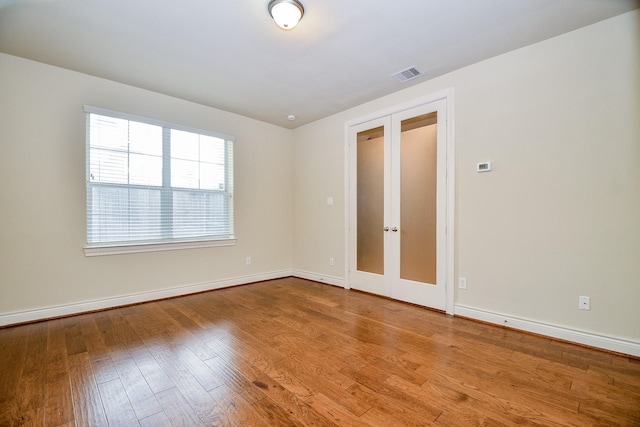 unfurnished room with visible vents, baseboards, wood finished floors, and french doors