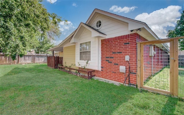 view of side of property with brick siding, a lawn, and fence