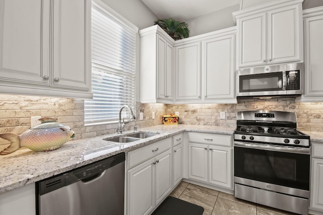 kitchen featuring a sink, white cabinetry, backsplash, appliances with stainless steel finishes, and light stone countertops