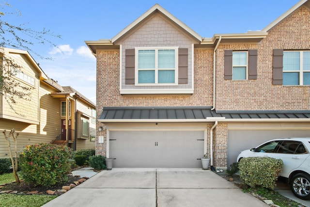 townhome / multi-family property with brick siding, driveway, a standing seam roof, and a garage