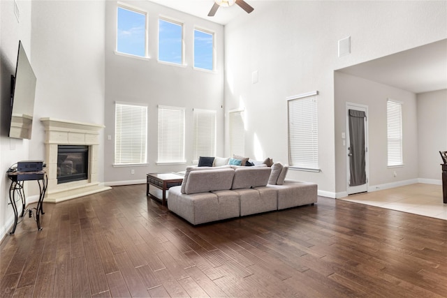 living area with a glass covered fireplace, wood finished floors, a ceiling fan, and baseboards