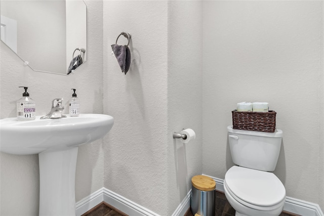 bathroom with a textured wall, toilet, baseboards, and a sink