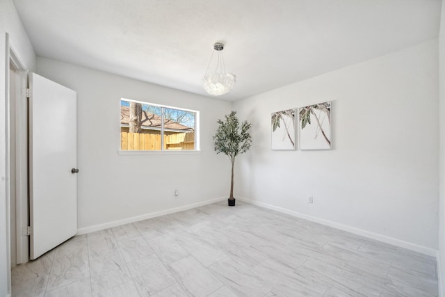 empty room with a notable chandelier and baseboards