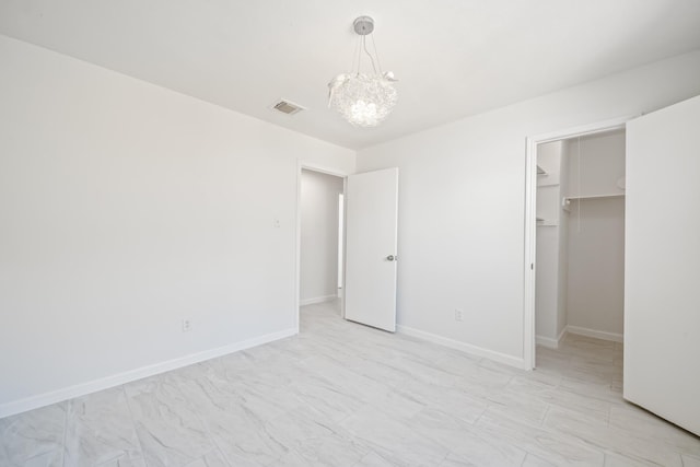 unfurnished bedroom featuring a spacious closet, visible vents, baseboards, a chandelier, and a closet