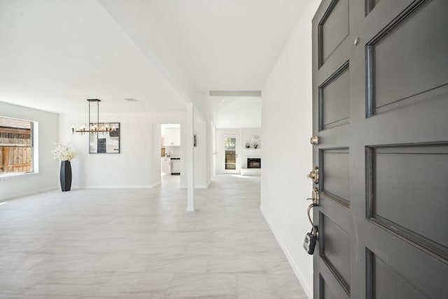 foyer featuring a fireplace, baseboards, marble finish floor, and a chandelier