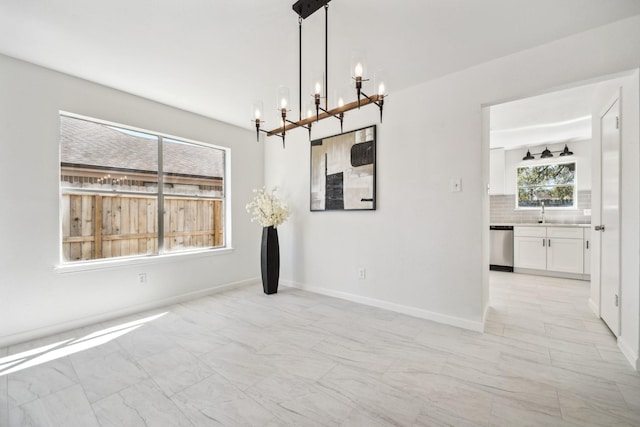 unfurnished dining area with an inviting chandelier, baseboards, marble finish floor, and a sink