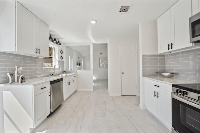 kitchen with visible vents, backsplash, stainless steel appliances, white cabinetry, and a sink