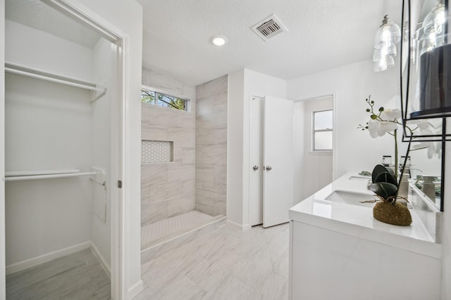 bathroom with visible vents, a textured ceiling, a spacious closet, and a tile shower