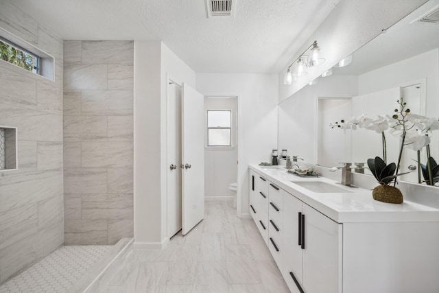 bathroom with a sink, toilet, a wealth of natural light, and a tile shower