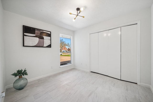 unfurnished bedroom featuring a closet, baseboards, and an inviting chandelier