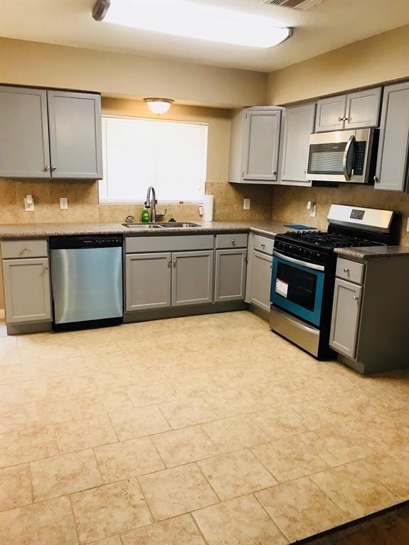 kitchen with decorative backsplash, gray cabinets, stainless steel appliances, and a sink