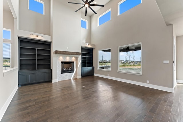 unfurnished living room featuring dark wood-style floors, baseboards, a fireplace, and ceiling fan