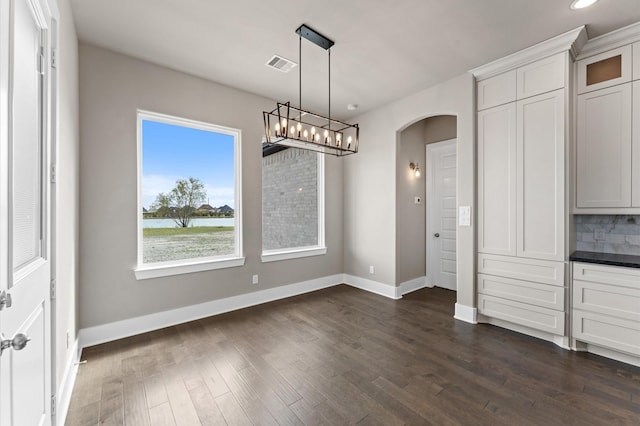unfurnished dining area featuring arched walkways, baseboards, dark wood-style floors, and visible vents