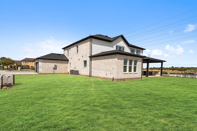 back of house featuring brick siding, fence, central AC, and a yard