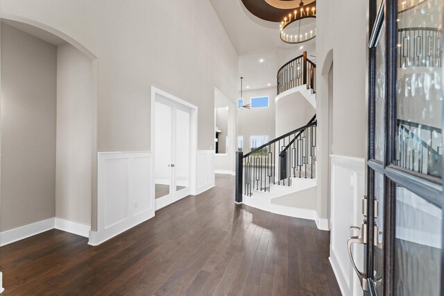 entrance foyer with stairway, a high ceiling, wood-type flooring, wainscoting, and arched walkways
