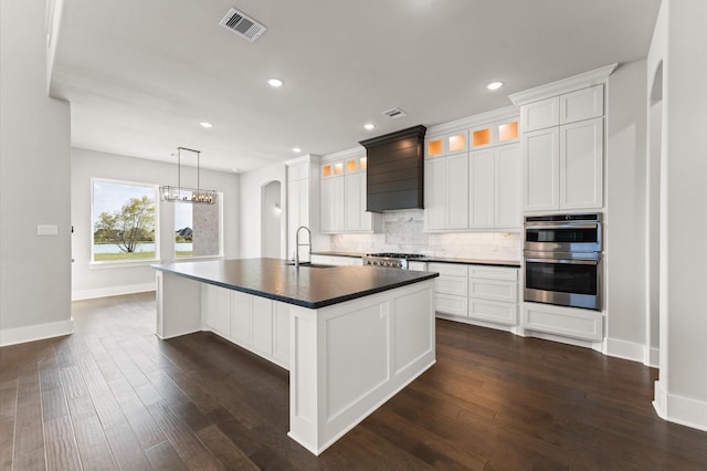 kitchen with backsplash, double oven, dark wood finished floors, dark countertops, and arched walkways