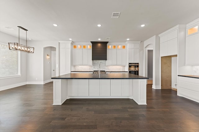 kitchen featuring arched walkways, stainless steel double oven, visible vents, and dark countertops