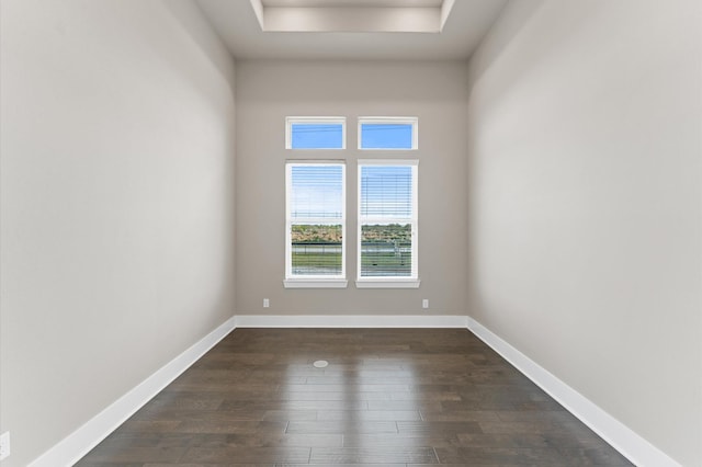 unfurnished room featuring a tray ceiling, baseboards, and dark wood finished floors