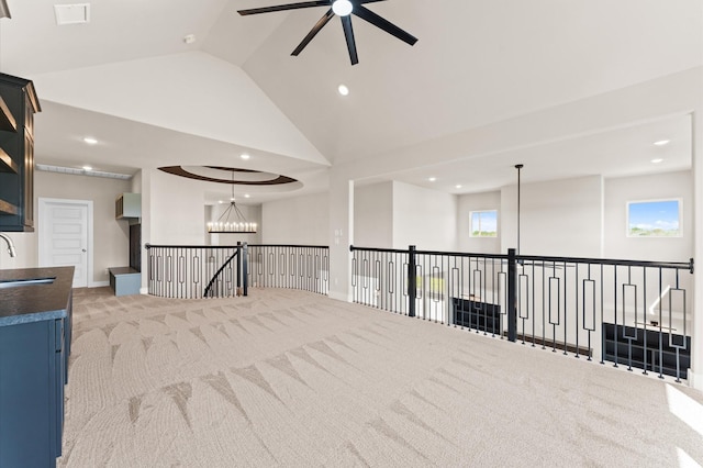 empty room featuring carpet flooring, high vaulted ceiling, ceiling fan with notable chandelier, a sink, and visible vents