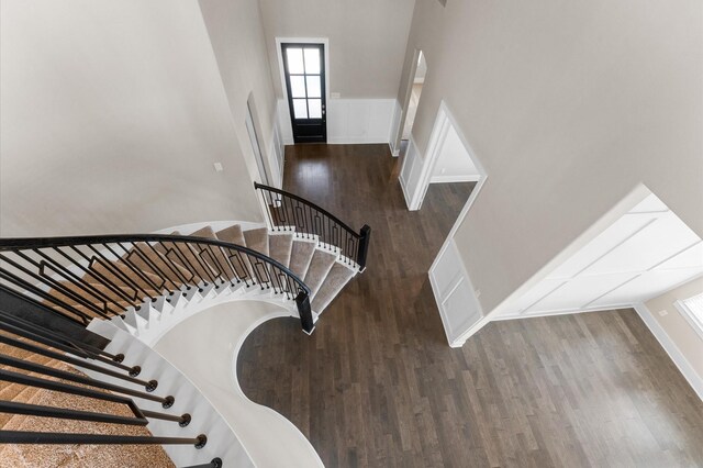 staircase featuring arched walkways, a high ceiling, and wood finished floors