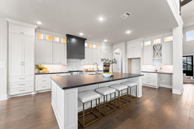 27003 Skiers Crossing Dr, Katy, TX 77493 - kitchen featuring wall chimney exhaust hood, dark countertops, arched walkways, decorative backsplash, and dark wood finished floors