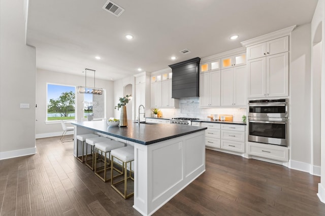 27003 Skiers Crossing Dr, Katy, TX 77493 - kitchen featuring double oven, dark countertops, decorative backsplash, a center island with sink, and premium range hood