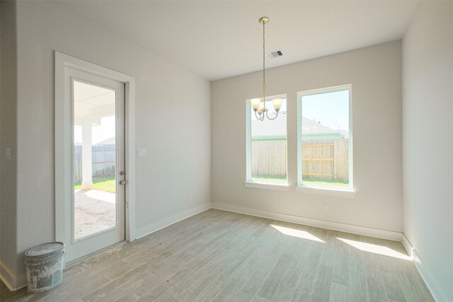 empty room with visible vents, light wood-style flooring, an inviting chandelier, and a wealth of natural light