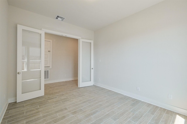 empty room featuring light wood-style floors, visible vents, baseboards, and french doors