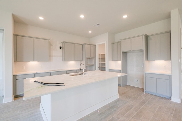 kitchen featuring a sink, gray cabinets, light wood-type flooring, and a kitchen island with sink