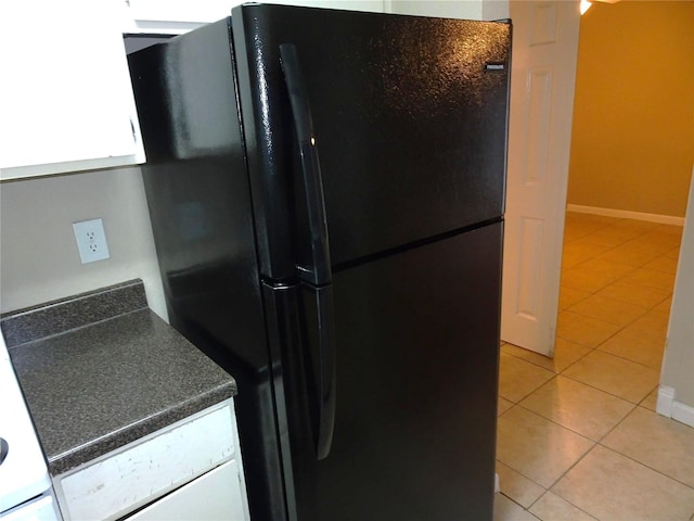 kitchen with dark countertops, baseboards, light tile patterned floors, freestanding refrigerator, and white cabinetry