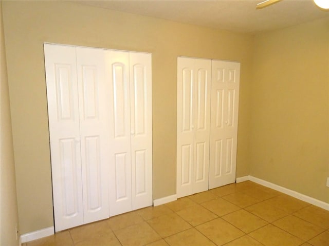 unfurnished bedroom featuring light tile patterned floors, baseboards, and two closets