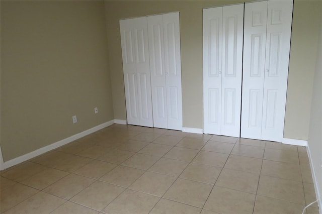 unfurnished bedroom featuring light tile patterned floors, two closets, and baseboards