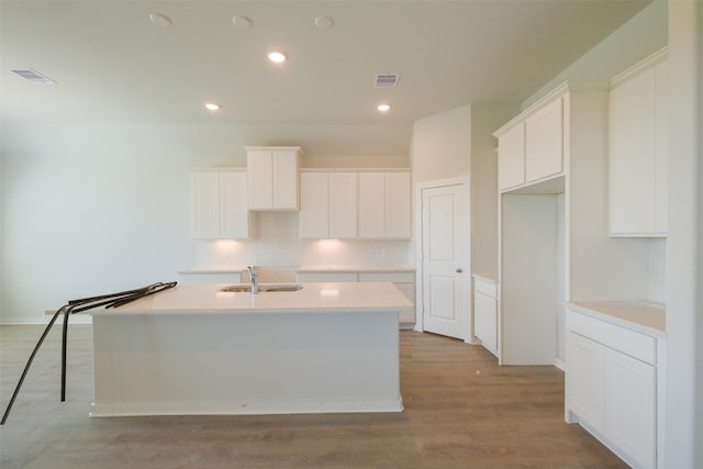 kitchen with light wood-style floors, an island with sink, a sink, and visible vents