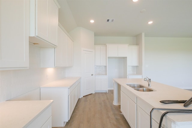 kitchen featuring white cabinetry, backsplash, light wood-style floors, a center island with sink, and a sink